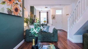 A living room with a green sofa, a coffee table with a bottle and glasses, and a painting of sunflowers on the wall. - NEW! Stylish City Centre Home, Great Location! (Chester)