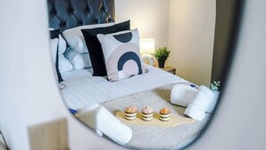 A neatly made bed with a tufted headboard, a bedside table with a lamp, and a small potted plant. - NEW! Stylish City Centre Home, Great Location! (Chester)