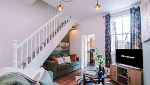A living room with a staircase, a sofa, a coffee table, and a TV. - NEW! Stylish City Centre Home, Great Location! (Chester)