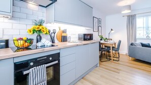 Une cuisine moderne avec des meubles gris, un four encastré et un coin repas comprenant une table et des chaises.