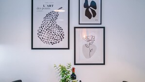 Trois œuvres d’art encadrées accrochées au mur, une plante en pot et une bouteille de vin.