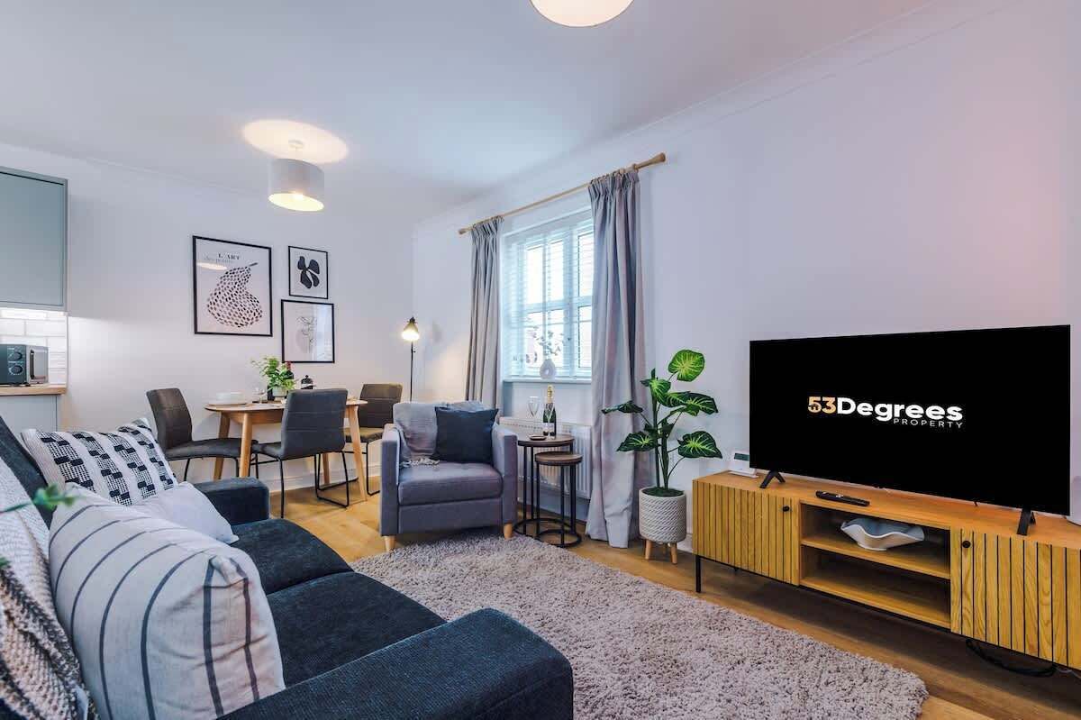 Un soggiorno moderno con divano, televisore, zona pranzo e un'ampia finestra con tende.