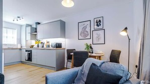 Une cuisine moderne avec des meubles gris, un coin repas avec une table et des chaises, et un salon avec un canapé et une lampe.