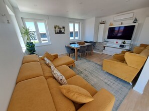 A modern living room with a sofa set, a dining area with chairs, a TV, and a small table.
