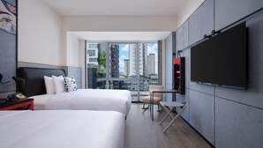 Et moderne hotelværelse med to senge, et fladskærms-tv, et lille bord og en stol.