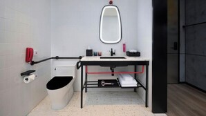 A modern bathroom with a white toilet, a black sink with a mirror above, a red telephone, and a trash bin. - Moxy Ningbo Old Bund (Ningbo)
