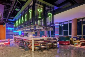 Un espace bar agrémenté d'enseignes au néon, d'un comptoir, de tabourets et d'un mur aux rayures colorées.