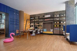 A modern room with a wooden floor, a desk with chairs, a bookshelf, and a pink flamingo decoration. - Moxy Ningbo Old Bund (Ningbo)