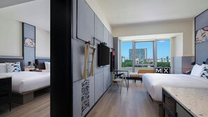 Une chambre d’hôtel avec deux lits, un bureau, une chaise, une télévision et de grandes fenêtres donnant sur la ville.