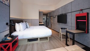 Une chambre d’hôtel moderne équipée d’un lit, d’une table de chevet, d’une chaise, d’une télévision et d’un petit bureau.