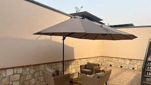 A patio area with wicker furniture and a large umbrella, set against a stone wall and a flat roof. - Le Cinèma (Formia)
