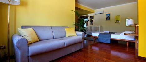 A living room with a sofa, a small table, a lamp, and a crib.