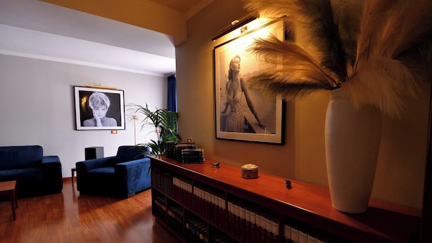 A modern living room with a wooden floor, blue sofas, a large vase with pampas grass, framed pictures on the wall, and a small table with books and a decorative item. - Le Cinèma (Formia)