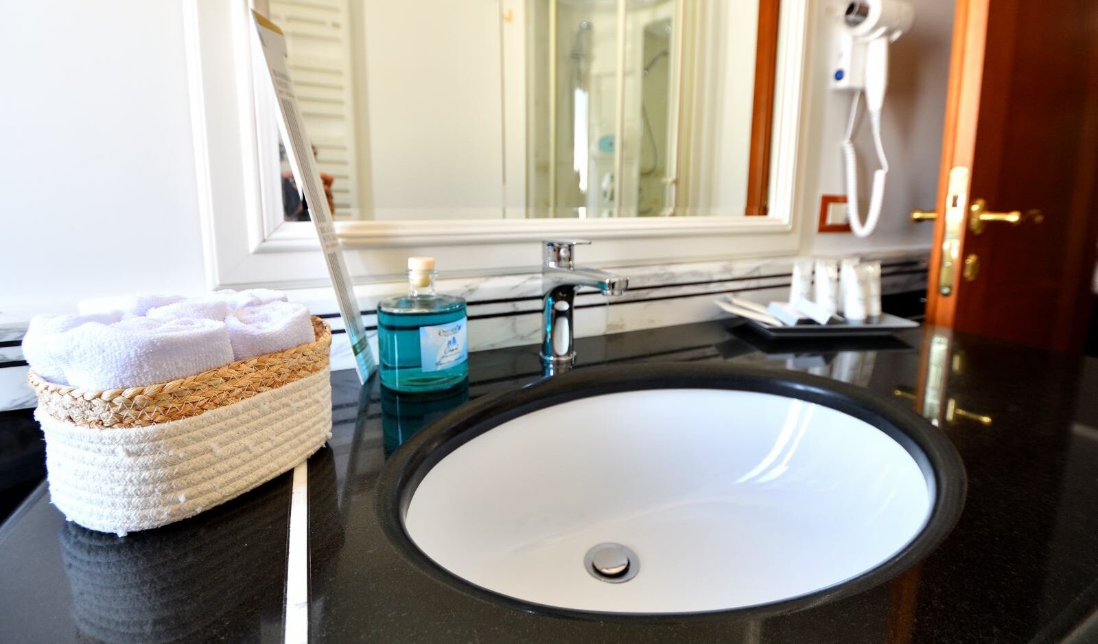 A bathroom with a white sink, a towel basket, and a mirror.