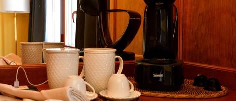 A coffee station with a coffee maker, cups, and a tea kettle on a wooden table.