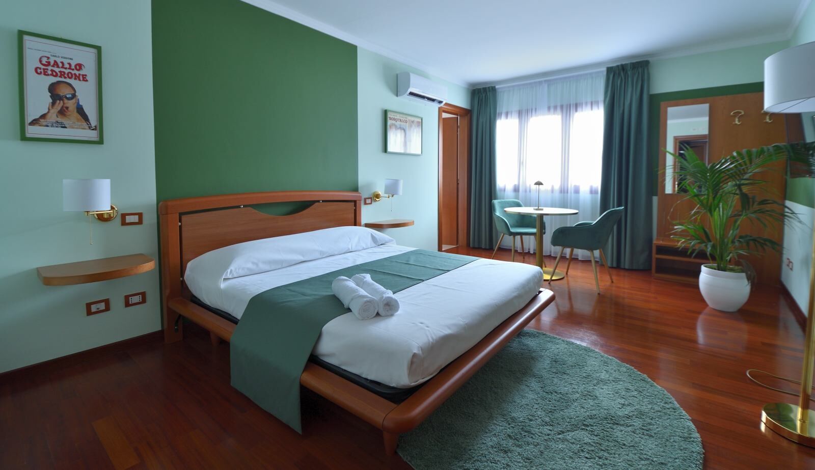 Ein Hotelzimmer mit einem hölzernen Bett, grünen Wänden, einem kleinen Schreibtisch und einem Topfpflanzen.