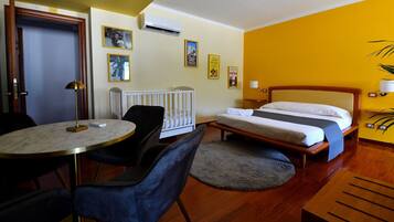A hotel room with a bed, a round table with chairs, a radiator, and wall decorations.