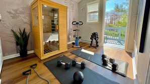 Ein Heimfitnessraum mit Trainingsmatten, Kurzhanteln, einem Rudergerät und einer Holzeinrichtung.