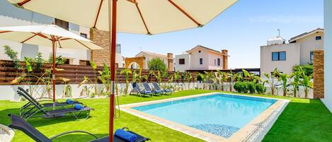 A swimming pool with lounge chairs and umbrellas, surrounded by well-maintained grass and plants.