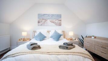 Un dormitorio con techo alto, una cama grande con dos almohadas, una mesita de noche con lámpara y un aparador de madera.