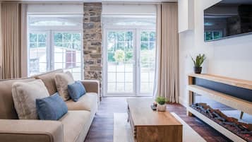 Una sala de estar moderna con un sofá beige, una mesa de centro de madera y un televisor montado en la pared.