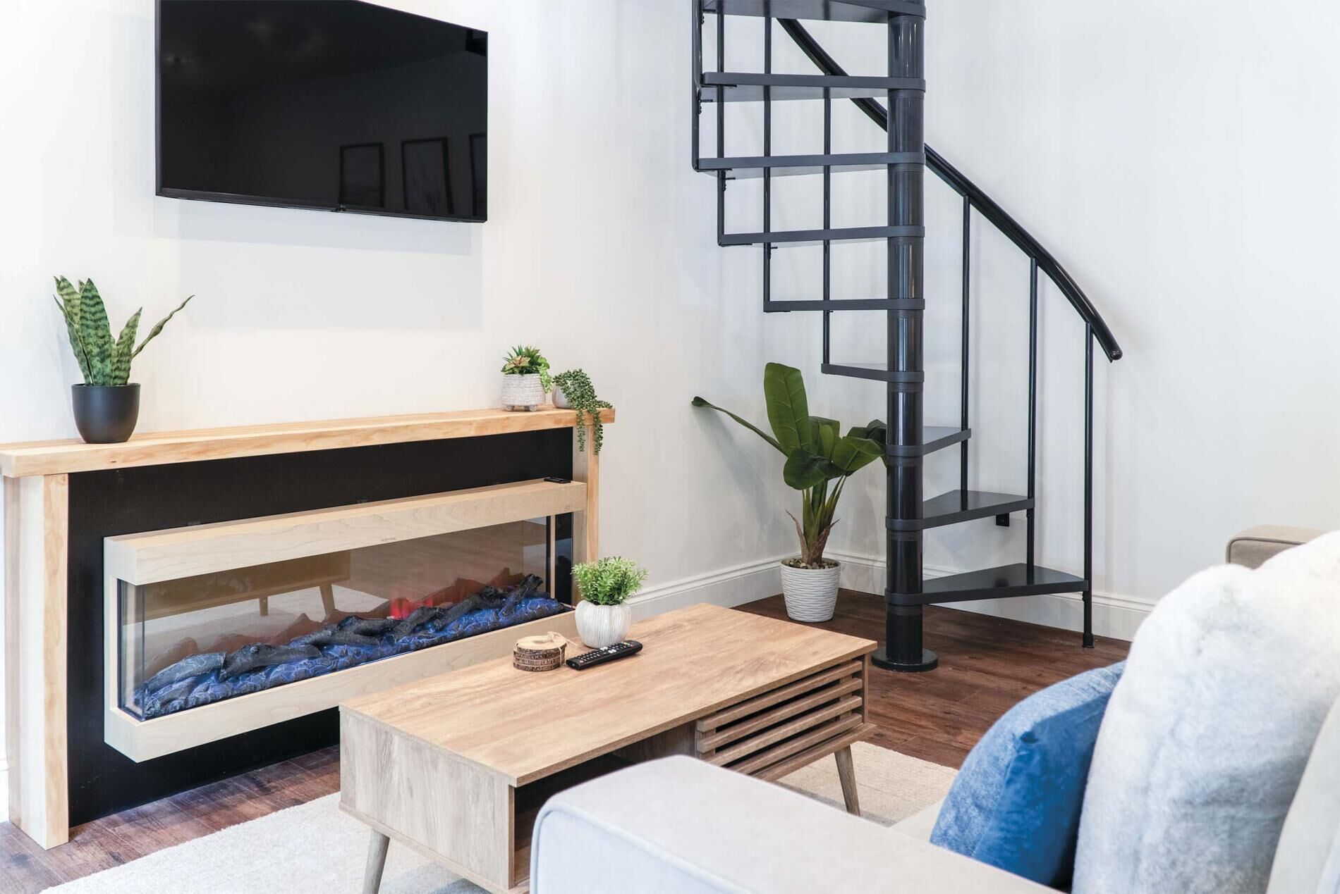 A modern living room with a fireplace, a wooden coffee table, a white sofa, and a black spiral staircase.