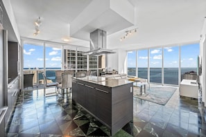 A modern kitchen with a large island, a dining area, and a view of the ocean.