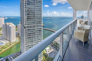 A high-rise building with a balcony featuring wicker furniture and a view of the ocean and other buildings. - Icon Brickell 2BDR 46th Fl Ocean & Pool Views (Miami)
