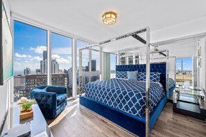A modern bedroom with a large bed, a glass desk, and a city view.