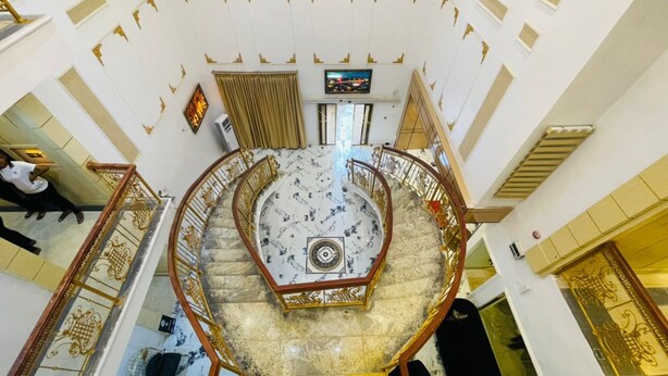 Una imponente escalera decorada, con piso de mármol y barandales dorados, que conduce a un nivel superior.
