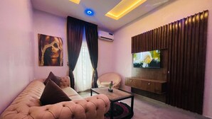 Una sala de estar moderna con un sofá capitonado, un televisor de pantalla plana, un mueble de madera y un panel decorativo en la pared.