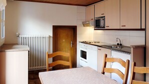 A compact kitchen with wooden cabinets, a microwave, an oven, and a dining table with chairs.