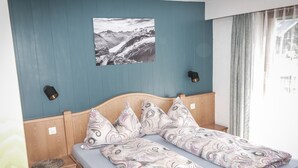 A bedroom with a bed, a nightstand, a wall-mounted lamp, and a window with curtains.