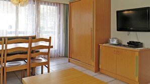 A room with a wooden dining table, chairs, a television, and a wardrobe.