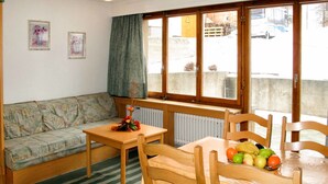 A cozy room with a sofa, a dining table with fruit, a radiator, and a window with a view of a building and a parked truck.