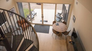 Ein geräumiges Zimmer mit großem Fenster, einer Holztreppe und einem Essbereich mit Tisch und Stühlen.