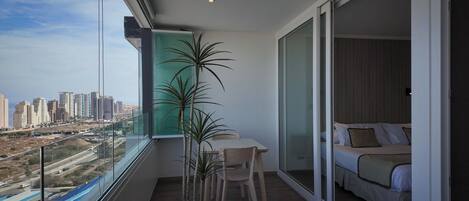 A balcony with a table and chairs, a bed, and a view of a cityscape.