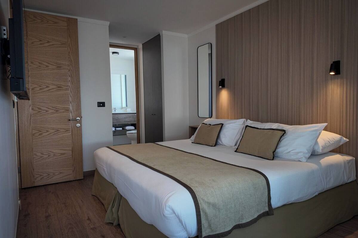 A hotel room with a bed, wooden paneling, a TV, a mirror, and a bedside table.