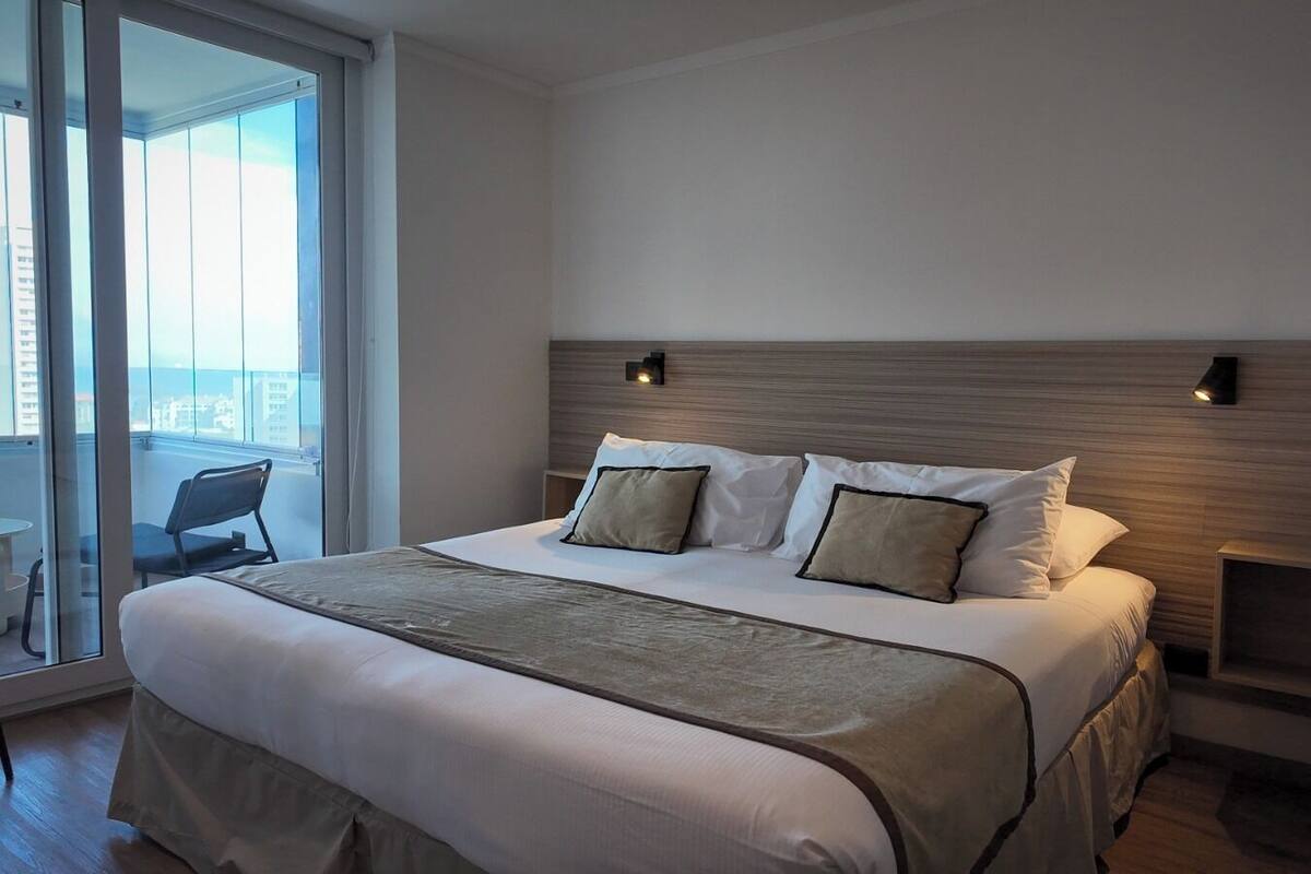 A modern hotel room with a large bed, a view of the city, and a balcony.
