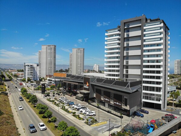 A modern building with multiple floors, a parking lot, and a road with vehicles.