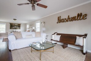 A living room with a white sofa, a glass coffee table, a wooden bench, and a ceiling fan. - The Franklin Farmhouse of Franklin, TN (Franklin)