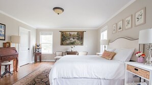Un dormitorio con una cama grande, un escritorio, una silla, una lámpara y un cuadro en la pared.