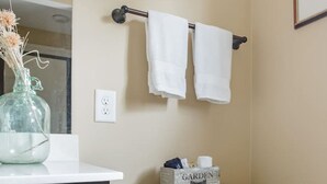Un baño con inodoro, lavamanos con un florero y toallero con dos toallas.