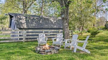 A rustic outdoor seating area with Adirondack chairs and a fire pit, surrounded by a wooden fence and trees.