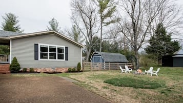 A single-story house with a front porch, a fenced yard, and a small outdoor seating area with chairs and a fire pit.