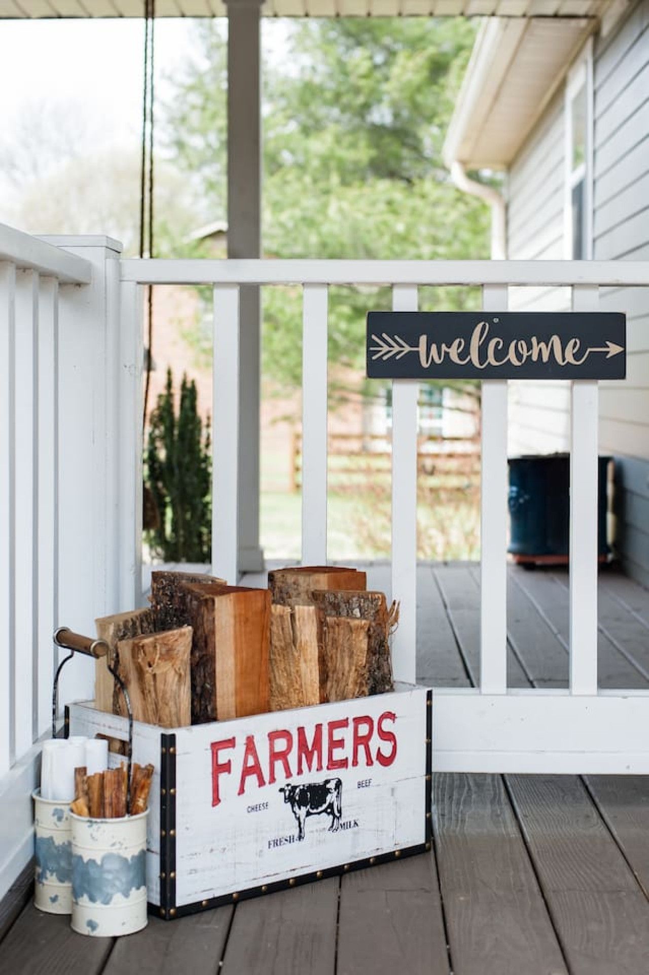 A wooden crate labeled "FARMERS" with wood logs and a "welcome" sign on a porch.