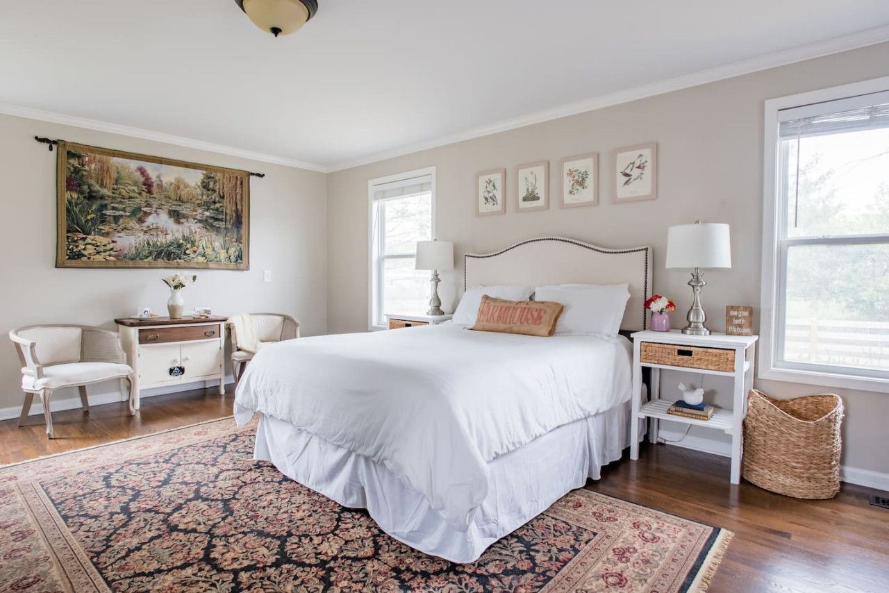 A bedroom with a large bed, a nightstand, a chair, a dresser, a painting, and a window.