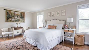 A bedroom with a large bed, a nightstand, a chair, a dresser, a painting, and a window.