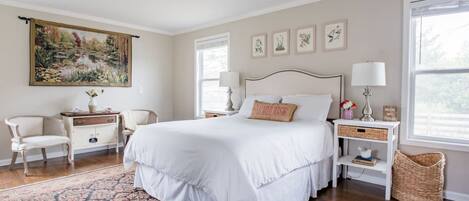 Une chambre à coucher avec un grand lit, une table de chevet, une chaise, une commode, un tableau et une fenêtre.