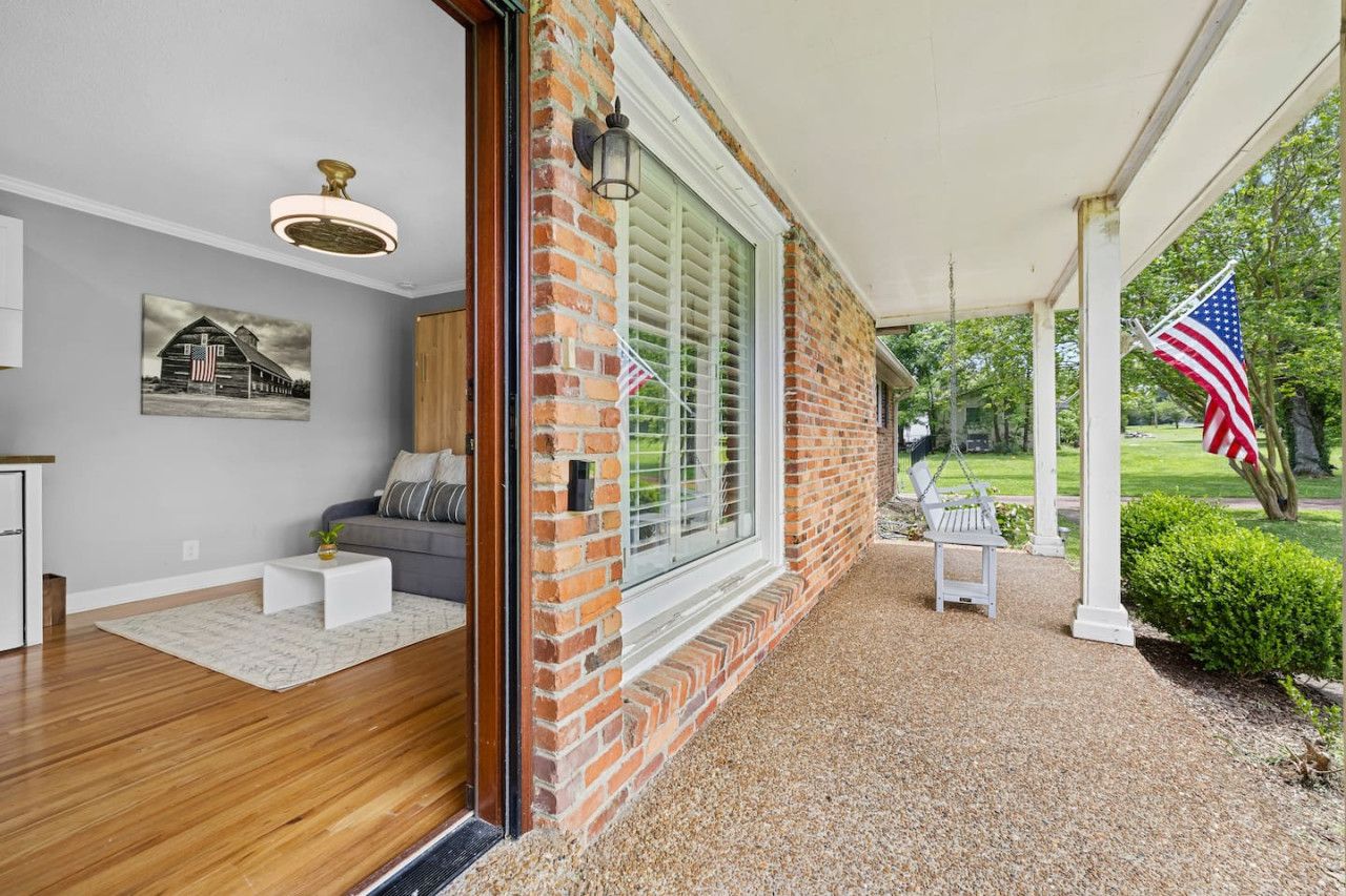 A covered porch with a brick wall, a white bench, and an American flag.